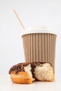 An half eaten doughnut and a cup of coffee placed together