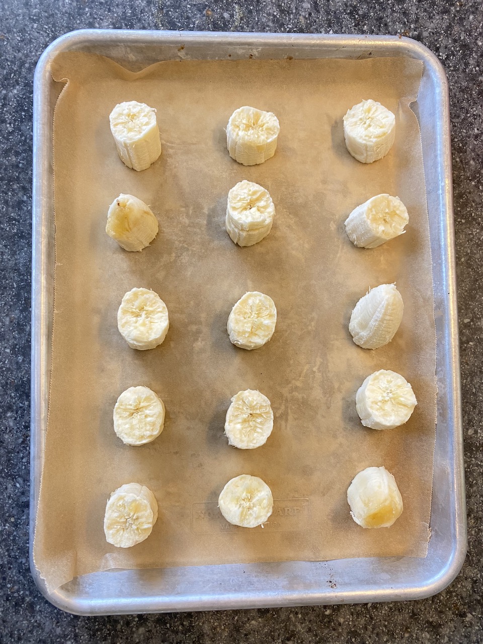 "quarter sheet pan with parchment paper and pieces of banana"