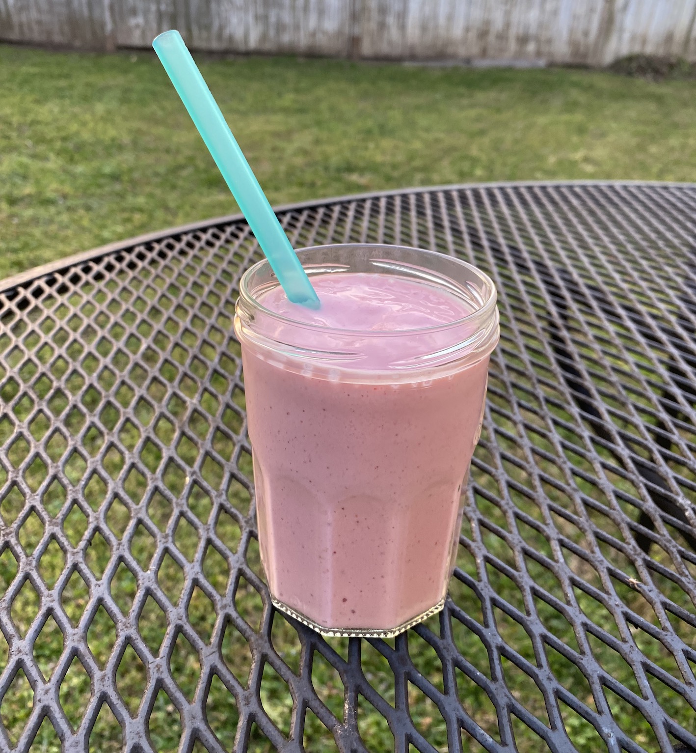 Strawberry and tahini smoothie in a clear glass on an outside table.