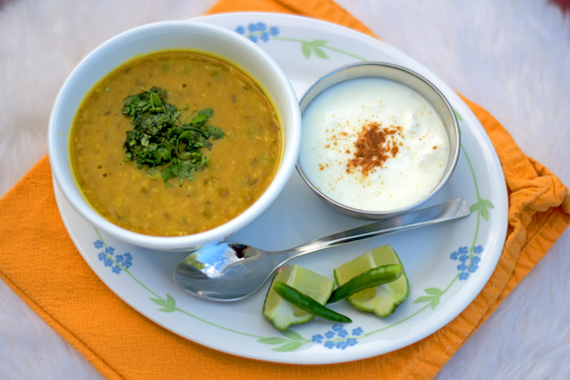 Indian dish served with a side of yogurt on a plate with a bright orange napkin. 