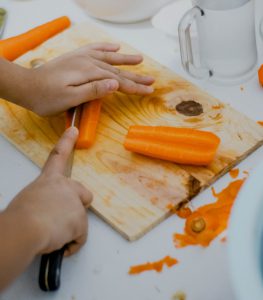 someone cutting a carrot lengthwise on a wooden cutting board with a chef's knife