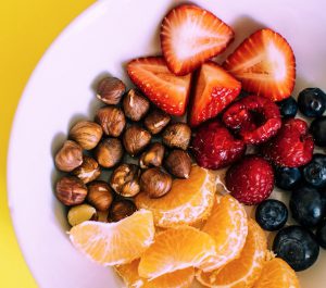 White plate full of fruit and nuts on a bright yellow background.