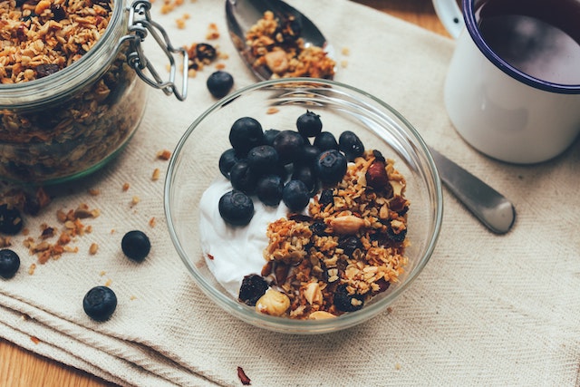 A bowl of yogurt and granola topped with blueberries and a cup of black coffee on a tablecloth.