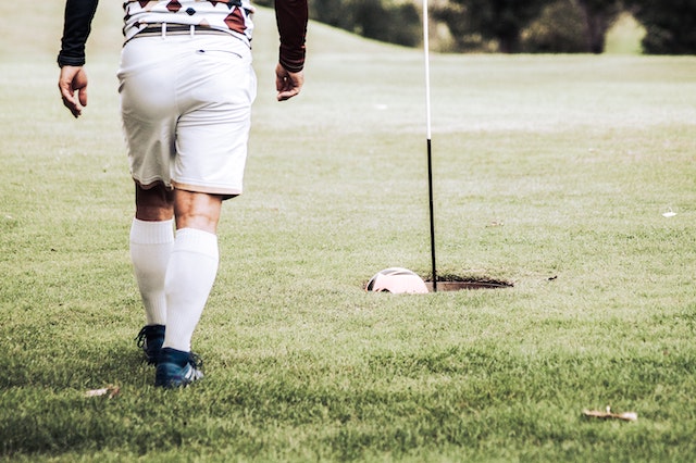 Man wearing soccer clothes walking towards a FootGolf hole to retrieve his soccer ball.