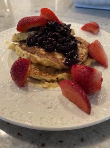 A white plate with a small stack of pancakes topped with fruit.