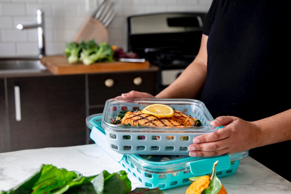 Person prepping leftovers into brightly colored containers in a kitchen.