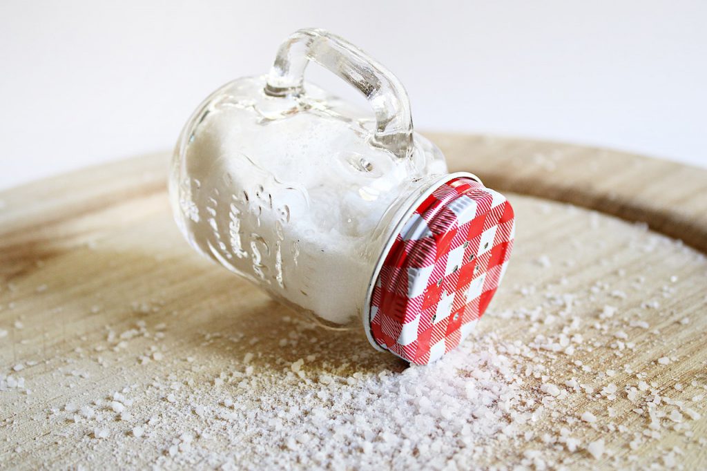 Vintage small mason jar salt shaker tipped over on a wooden table