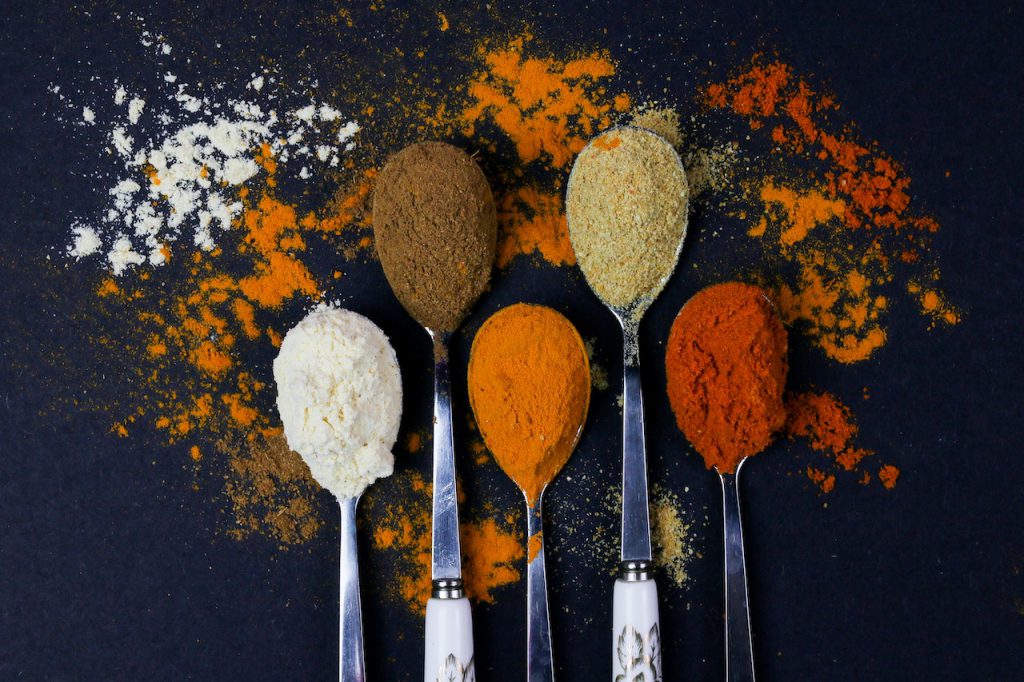 5 spoons filled with brightly colored spices on a black background