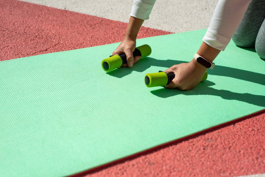 green dumbbells in hands on green mat