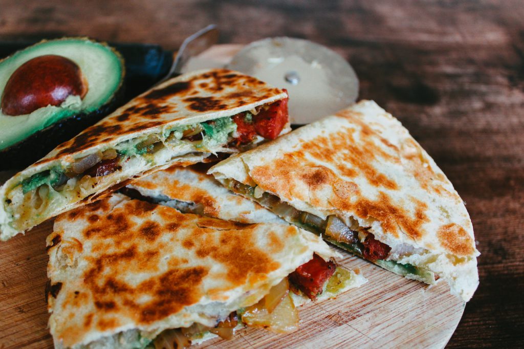 crispy vegetable quesadilla on a wooden cutting board with an avocado on the side