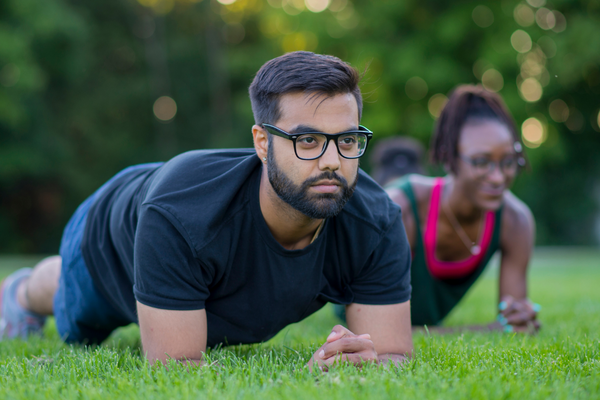 Young man and woman doing planks in a park with a group exercise class.
