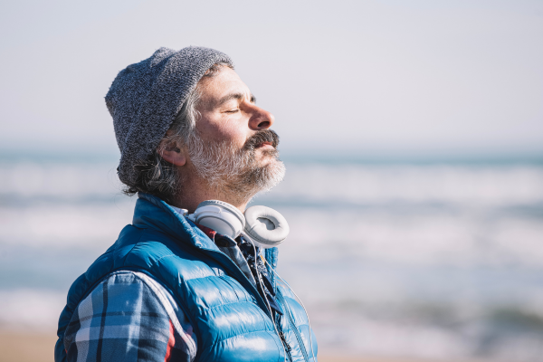 Man in winter clothes taking a deep breath while outside on a walk. 