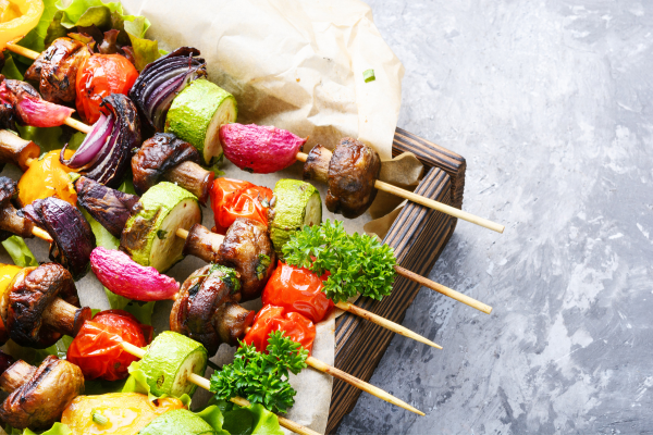 Image of grilled vegetables on sticks sitting on a tray lined up. 