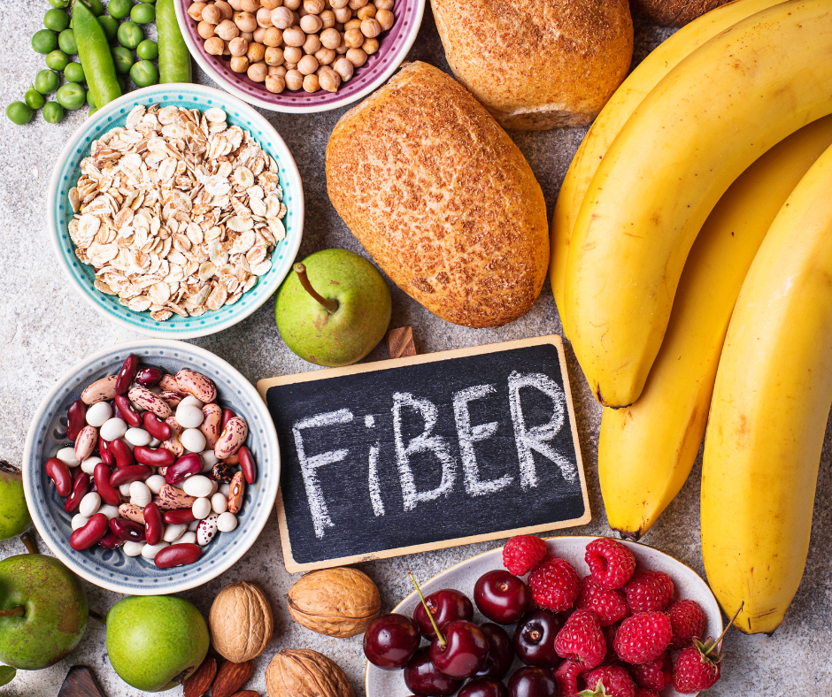 Assorted high-fiber foods including fruits, nuts, beans, and whole grains surrounding a chalkboard labeled "fiber".